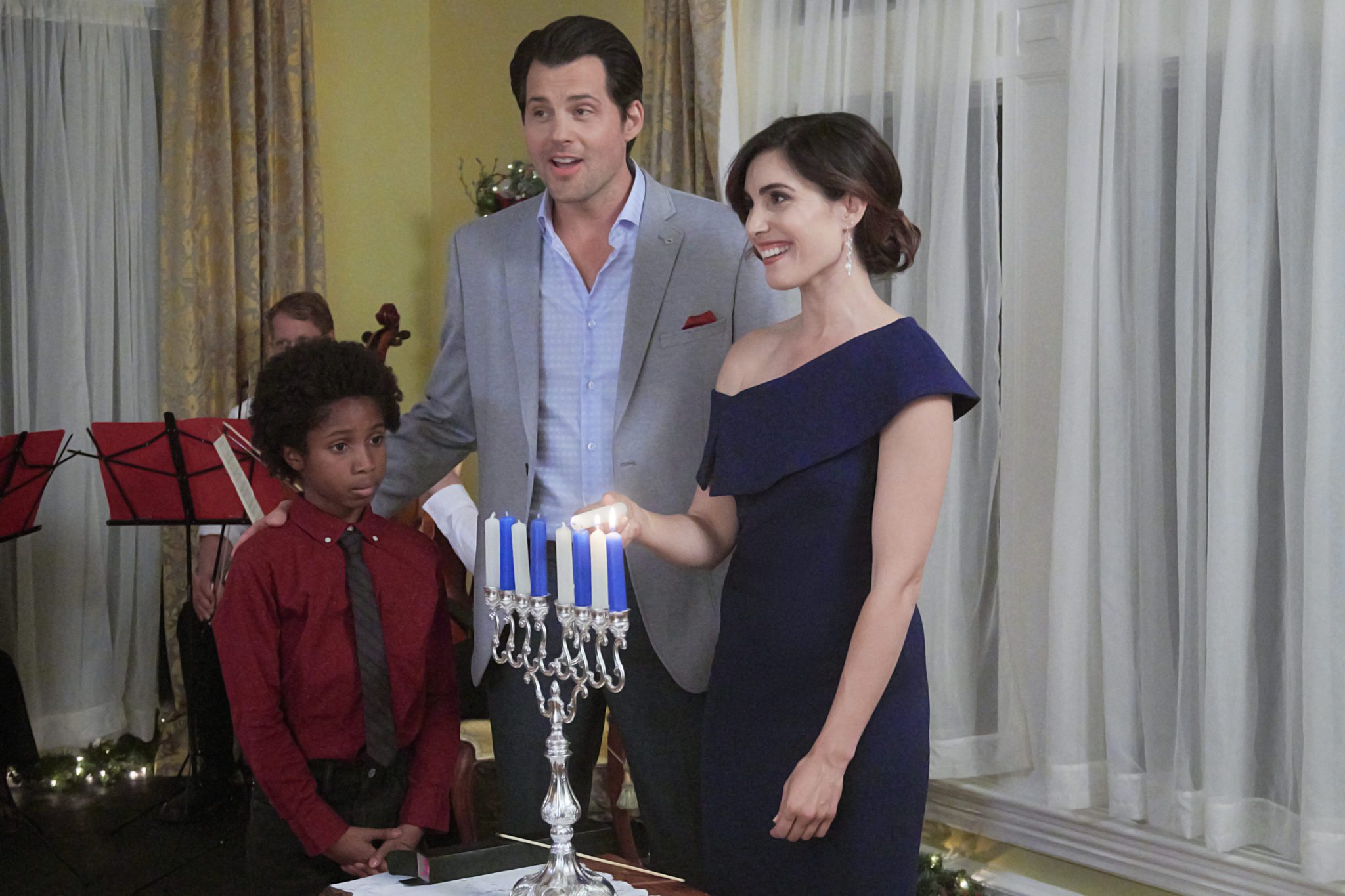 Career-minded Rebecca’s plans for Hanukkah go askew when a promotion opportunity comes up at work. When the company CEO asks Rebecca and her insufferable office mate, Chris – also her main competitor for the promotion – to plan the company’s Christmas party, she realizes they must overcome their opposing styles in order to succeed. Forced to work together on the holiday party, Chris learns more about Rebecca and her family’s Hanukkah traditions, while she also begins to see him in a new light. Although feelings slowly develop between the two, the ongoing competition over the promotion threatens to undermine it all. Photo: Ceyon Crossfield, Kristoffer Polaha, Carly Pope Credit: ©2019 Crown Media United States LLC/Photographer: Albert Camicioli
