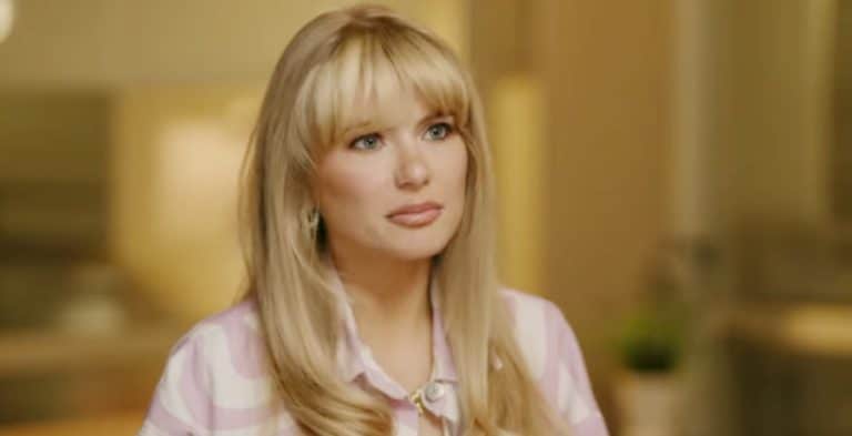 A woman with blonde hair in a light pink shirt.